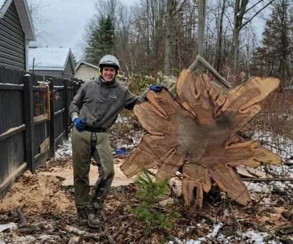 Joel Thompson of Kingdom Tree Company beside a large trunk section from a completed tree removal